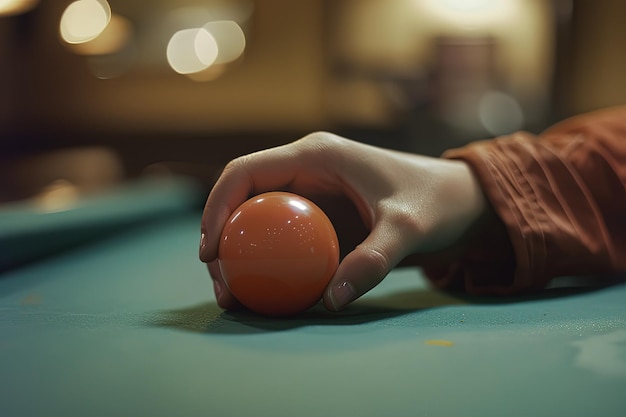 A persons hand holding an orange ball on a pool table