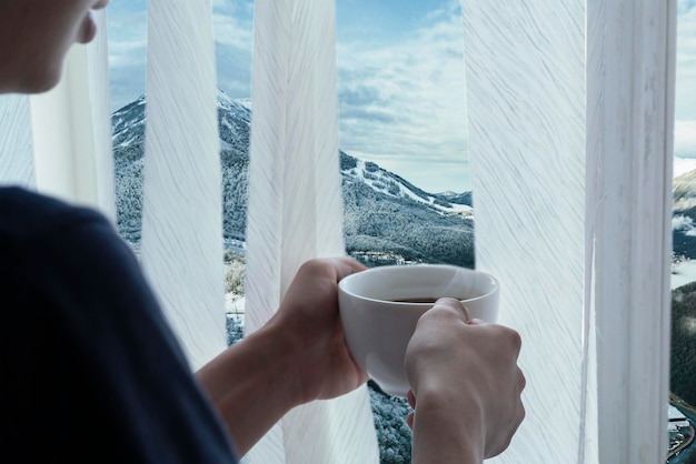 persons hands hold cup of hot coffe opposite from the window at winter season b