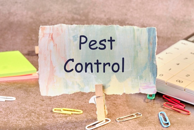 PEST CONTROL phrase written on paper next to scattered paper clips calculator adhesive paper