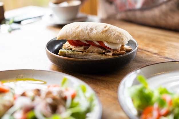 Pesto sandwich with chicken tomatos and mozzarella on the table in summer restaurant natural light