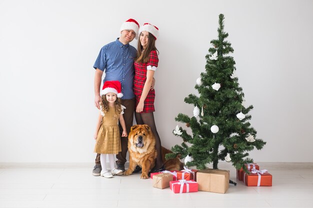 Pet, holidays and festive concept - Family with dog are standing near christmas tree.