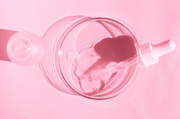 Petri dish With transparent gel With a pipette Cosmetics bottle On a pink background