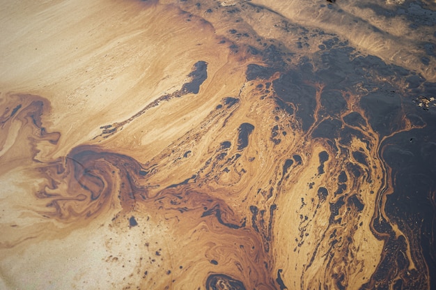 Petroleum spill mixed with other chemical substances on sea and sand surface. 