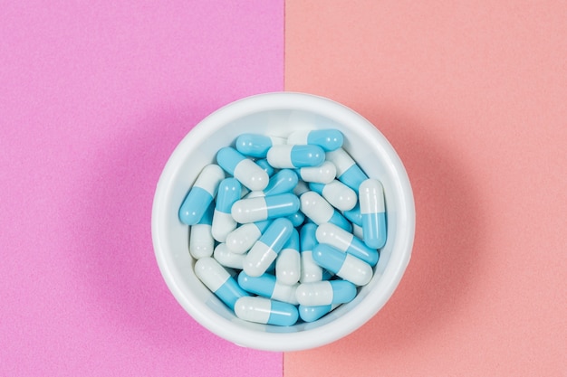 Pharmaceutical medicine pill capsules, in plastic bowl on colorful pink wall.