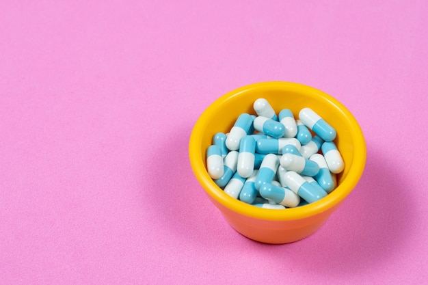 Pharmaceutical medicine pill capsules, in plastic bowl on colorful pink wall.