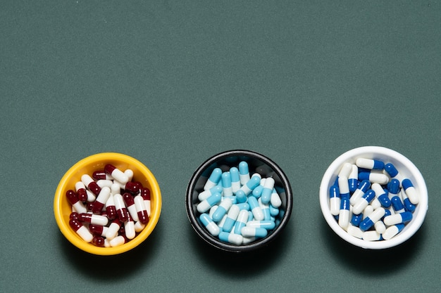 Pharmaceutical medicine pill capsules, in plastic bowl on  grey wall