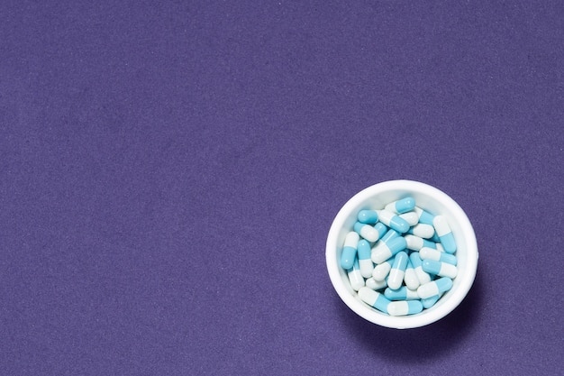 Pharmaceutical medicine pill capsules in plastic bowl on purple background