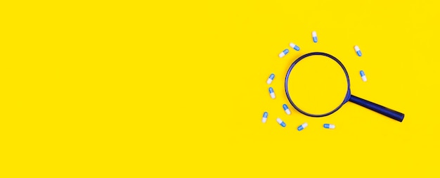 Pharmaceutical tablets and capsules near a magnifying glass on a yellow background View from above Concepts of medicine Minimalistic abstract concept Antibiotics painkillers vitamins Banner