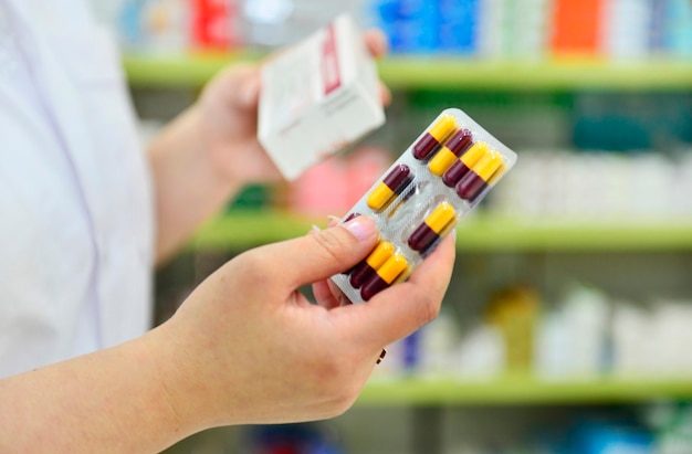 Pharmacist holding capsule pack and medicine box in pharmacy drugstore.