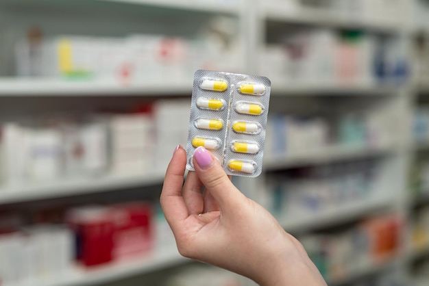 Pharmacist's hand holding many different pills near the chest of shelves with medicines