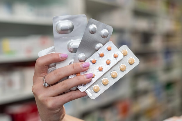 Pharmacist's hand holding many different pills near the chest of shelves with medicines