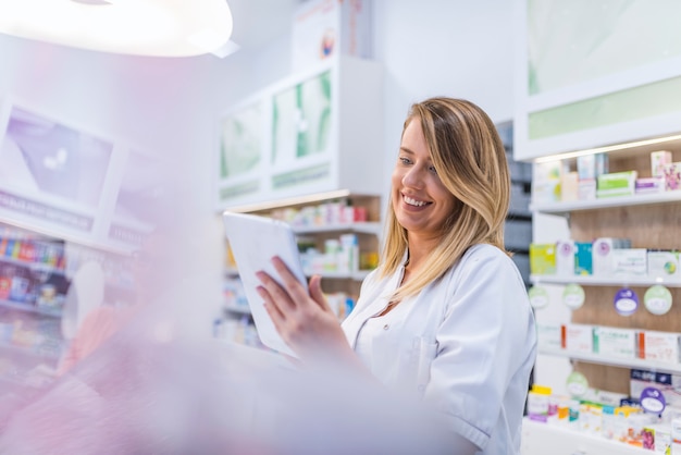 Pharmacist working with a tablet in the pharmacy holding it in her hand while reading info