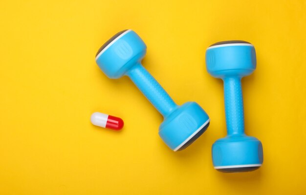 Pharmacology in sports. Dumbbell and capsule on a yellow background. Vitamins, steroids. Top view