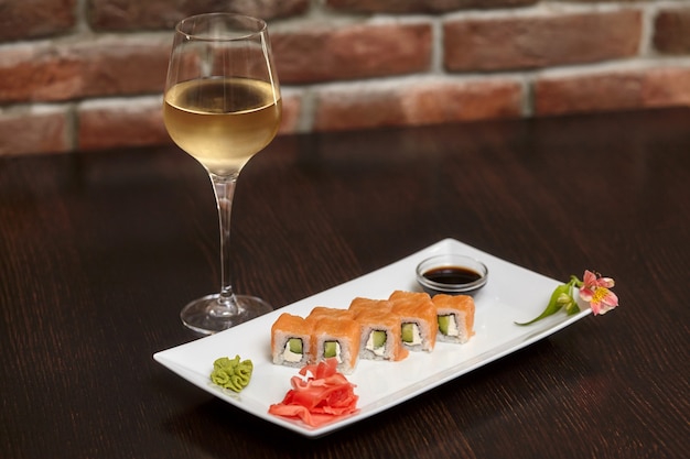 Philadelphia maki sushi rolls with salmon, cheese cream, cucumber on white plate and glass of wine