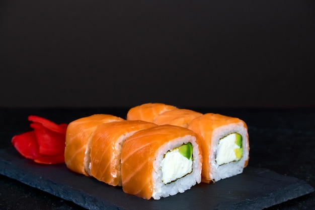 Philadelphia rolls with salmon fish avocado and cream cheese on stone plate on dark background