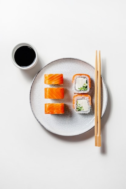 Philadelphia rolls with salmon fish, cucumber and cheese on plate with soy sauce on white background