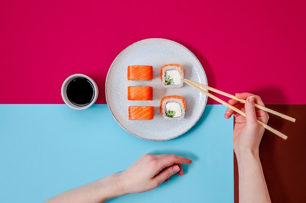 Philadelphia rolls with salmon fish cucumber and cheese on plate and woman hand with chopsticks on colorful background