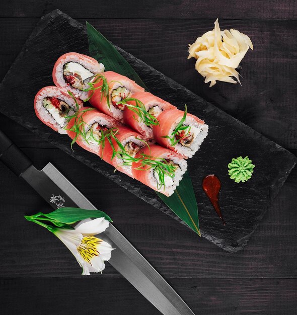 Photo philadelphia sushi rolls lying on black stone plate with knife and flower