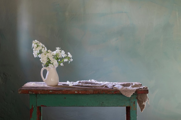 Phloxes in vase on old wooden table on green background