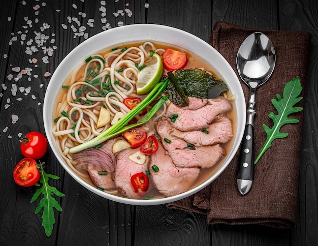 Pho Bo Soup with beef rice noodles chili pepper in bowl on black background