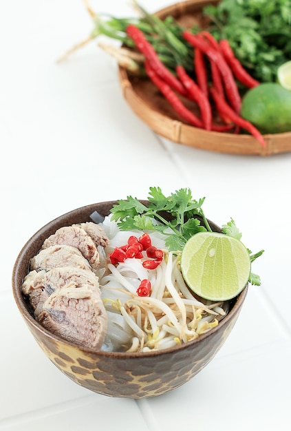 Pho Bo Soup with Beef Rice Noodles Lime Chili Pepper amd Sprout in Bwon Bowl on White Background