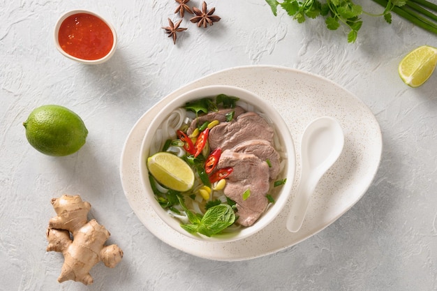 Pho Bo traditional Soup with beef rice noodles ginger lime chili pepper in bowl on white background View from above Vietnamese and Asian cuisine