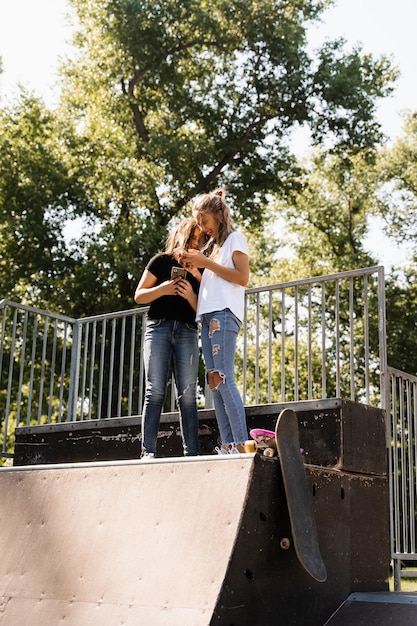 Phone addicted sports children with skateboard and penny boards use phones instead of skating and play together Children looking at smartphones on sports ramp Kids addiction of phones