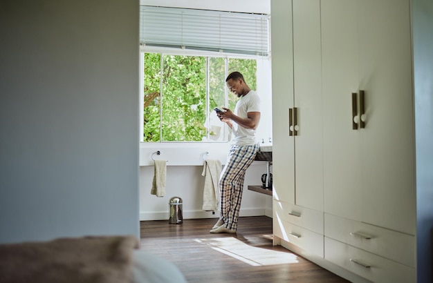 Phone bathroom and black man in home on social media texting or internet browsing Relax cellphone or happy male holding mobile smartphone for web scrolling networking or messaging alone in house