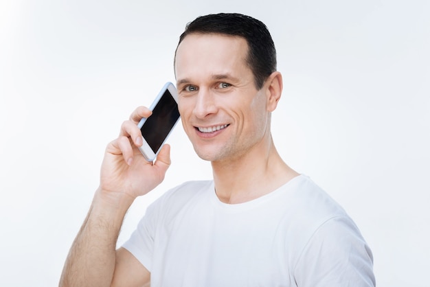 Phone call. Joyful nice pleasant man holding his smartphone and looking at you while making a phone call