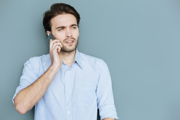 Phone communication. Smart nice confident man standing and putting a phone to his ear while making a call