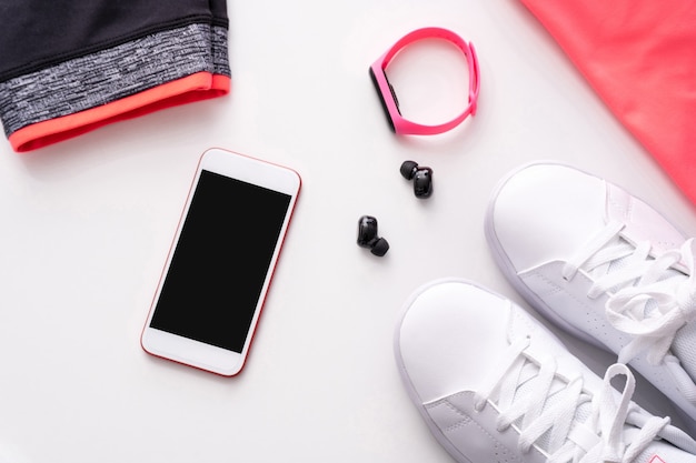 Phone, headphones, watch with sportswear and sneakers on white background