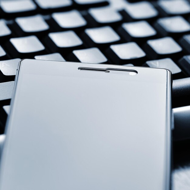 A phone laying on top of a keyboard with the letters t on it