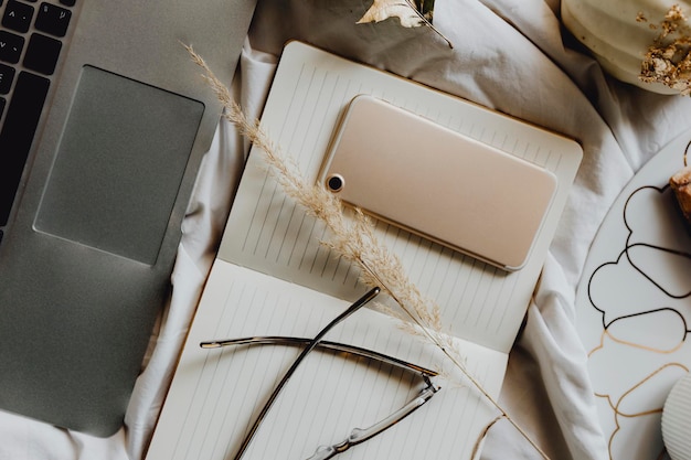 Phone on a notepad next to laptop on a bed