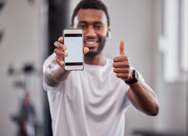 Phone screen mockup and black man with thumbs up in gym for exercise or fitness Sports portrait and male athlete with smartphone for branding advertising or marketing with hand emoji for success