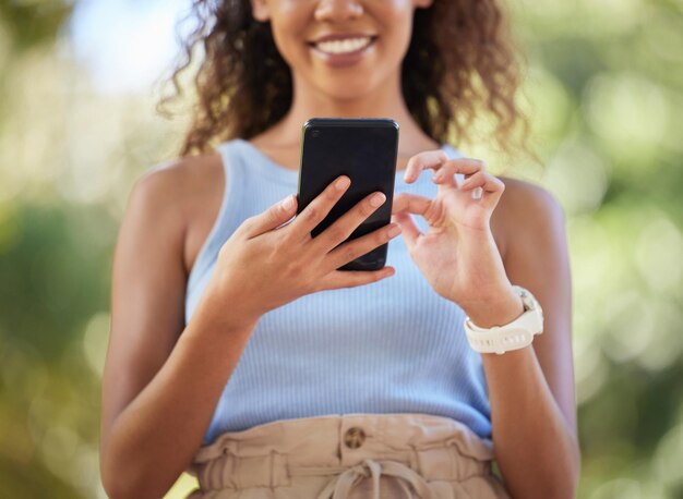 Phone social media and woman online texting on the internet web or app outdoors in a park Closeup mobile and surfing on a website by a happy person connecting due digital communication