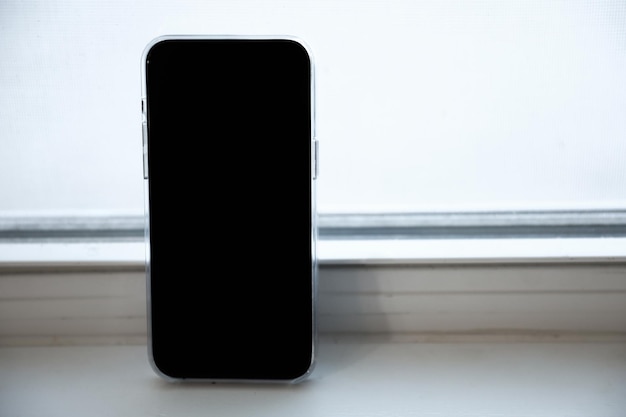 A phone with a blank screen sits on a window sill.