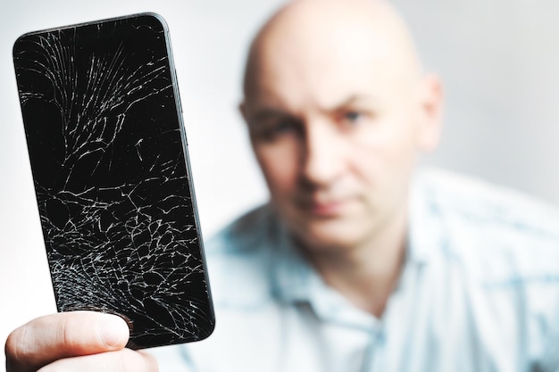 Phone With A broken screen closeup A white man is holding a black smartphone with a cracked display