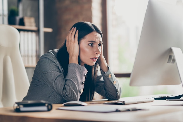 Photo of afraid scared girl work remote computer pc touch hands head frustrated about job loss boss crisis covid notification wear blazer jacket sit table desk in workplace workstation