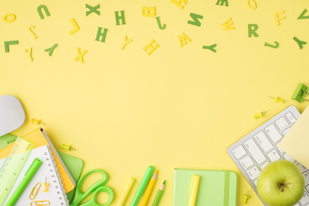 Above photo of alphabet letters notebook pen pencil felttip scissors ruler paperclips apple computer mouse and keyboard isolated on the yellow background with empty space