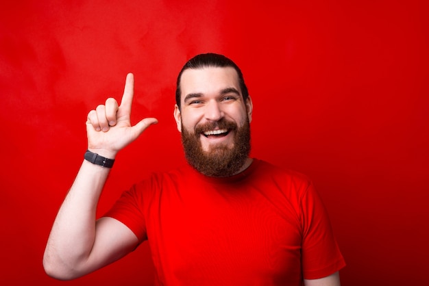 Photo of amazed bearded man pointing up over red wall