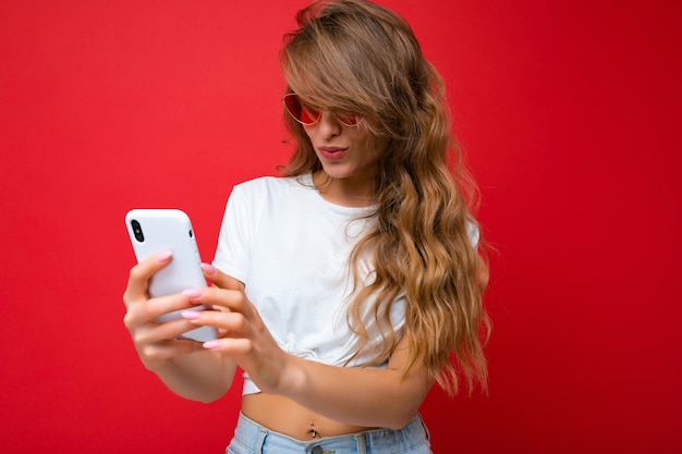 Photo of amazed beautiful young woman holding mobile phone wearing sunglasses everyday stylish