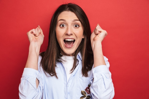 Photo of an amazing surprised emotional young beautiful woman posing isolated over red wall wall.