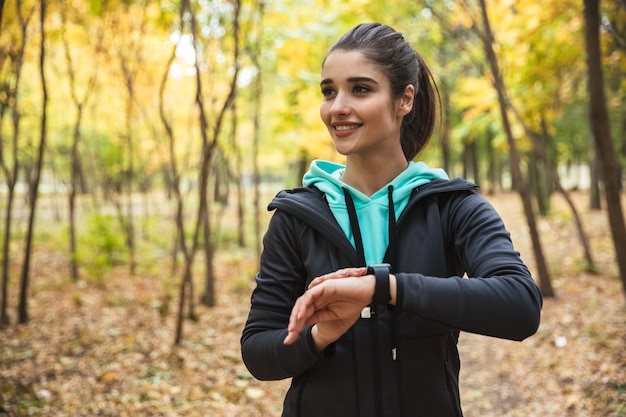 Photo of amazing young pretty fitness woman outdoors in the park looking at watch clock.