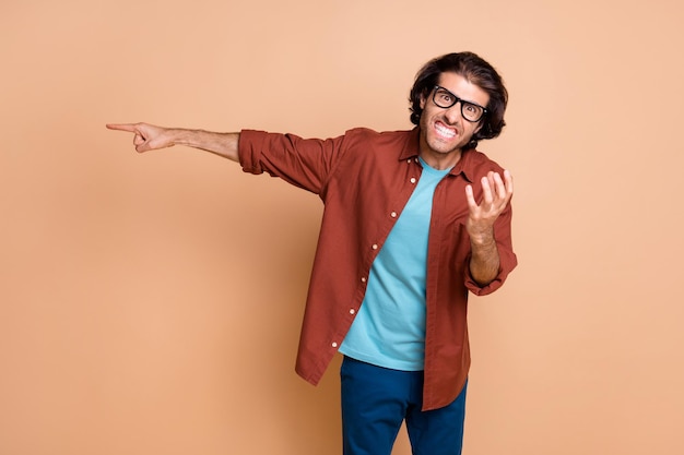 Photo of angry irritated man direct finger away wear glasses brown t-shirt isolated beige color background