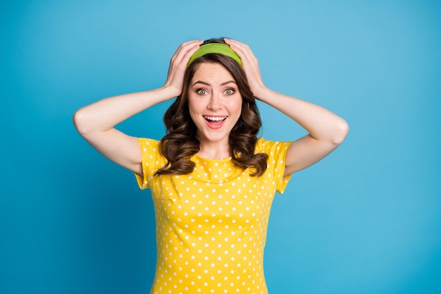 Photo of astonished crazy young girl touch hands head shout loud isolated over blue color background