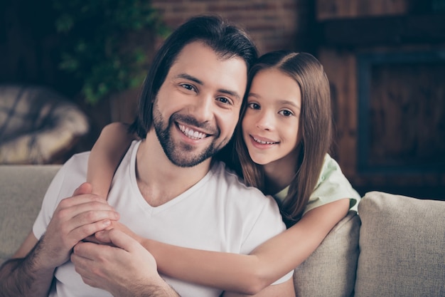 Photo of beautiful little adorable girl and handsome young daddy sit on comfy sofa