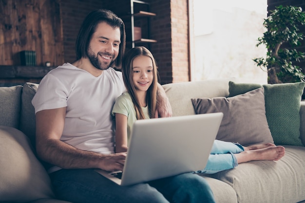 Photo of beautiful little adorable girl and handsome young daddy sit on comfy sofa