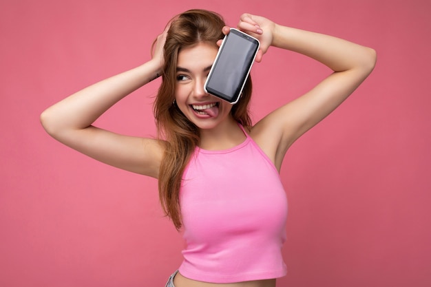 Photo of beautiful positive young blonde woman wearing pink top poising isolated on pink background