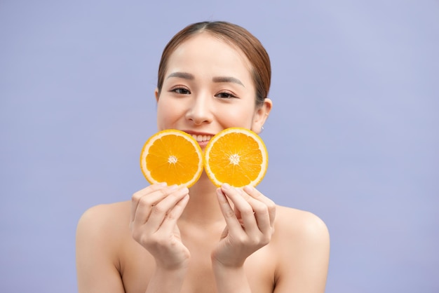 Photo of a beautiful woman holding oranges posing isolated over violet background