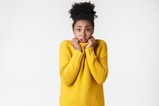 Photo of a beautiful young emotional frozen woman in sweater posing over white wall.